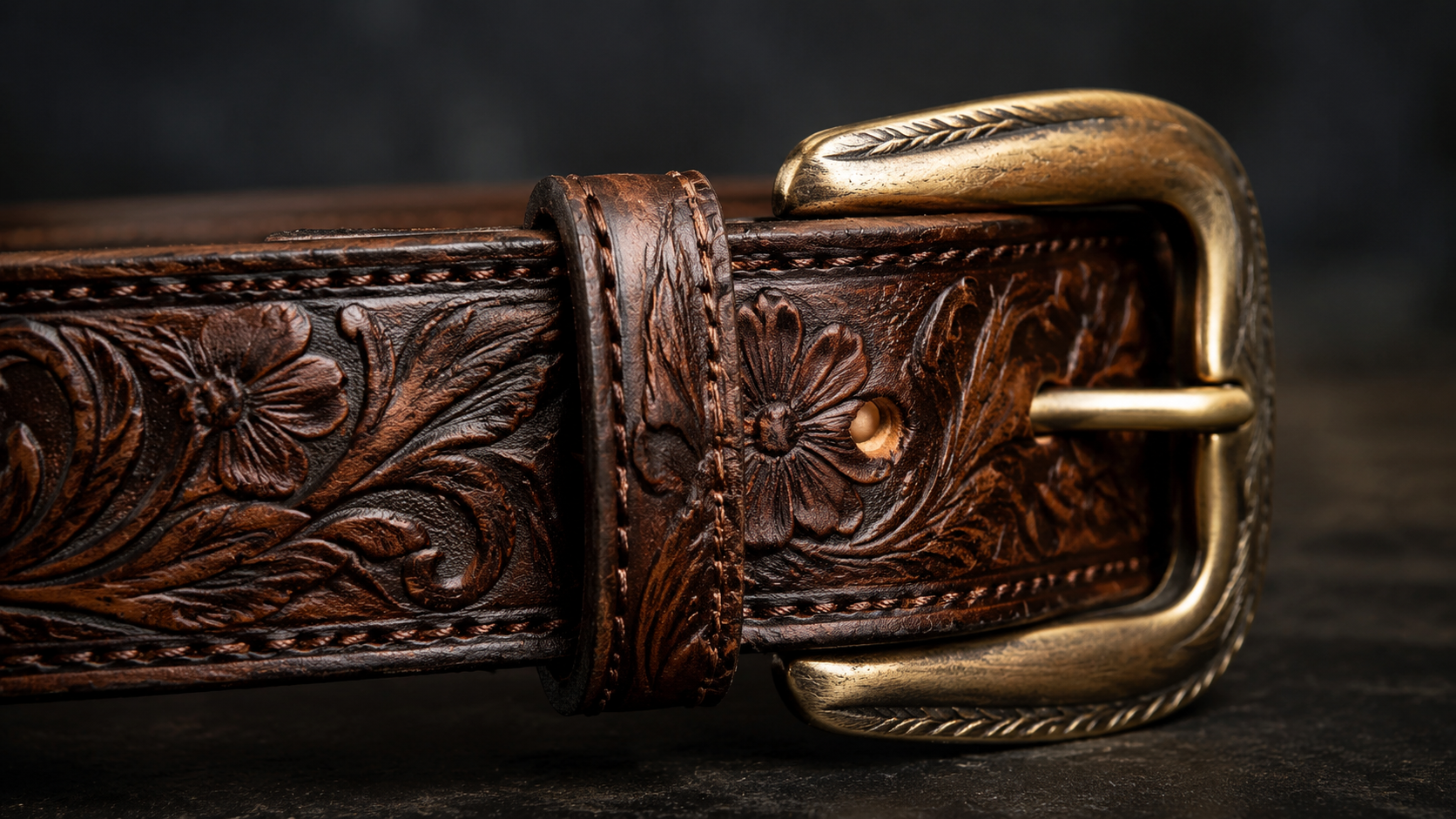 Macro close-up of western leather belt showing hand-tooled floral pattern and polished brass buckle detail