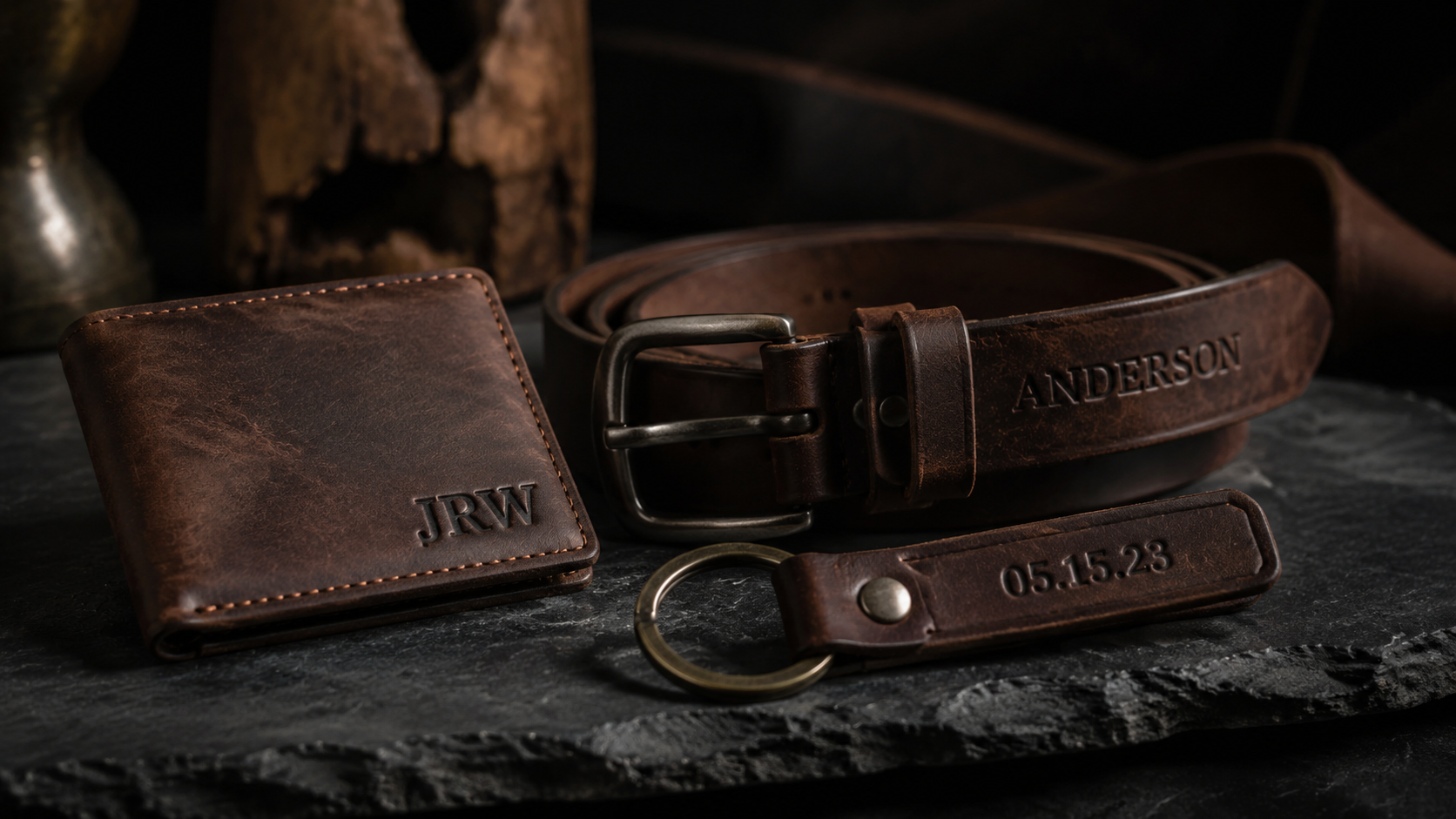 Three personalized engraved leather gifts on dark slate showing custom initials and dates